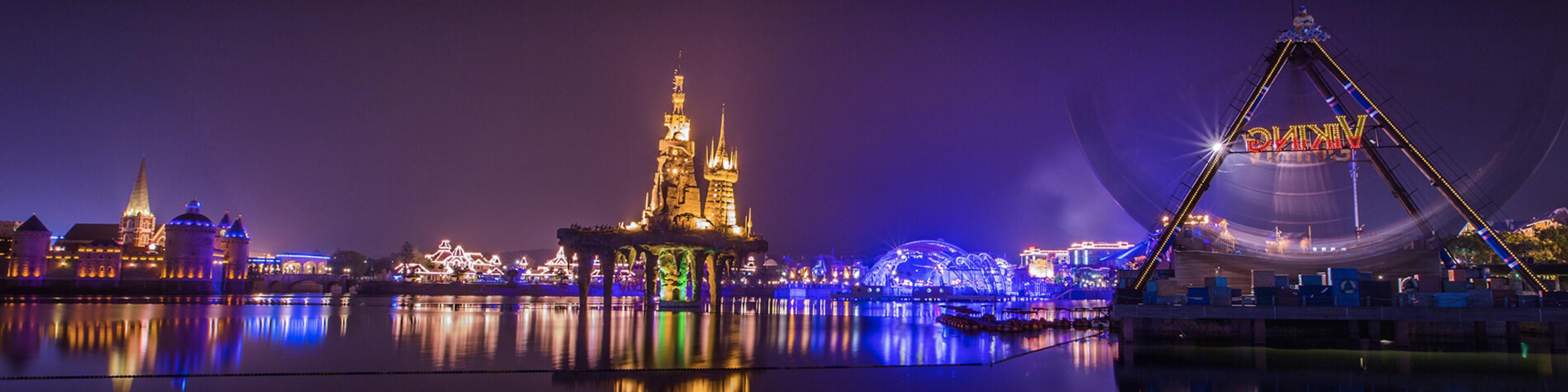 Discoveryland theme park at night with illuminated castle and lake, Dalian
