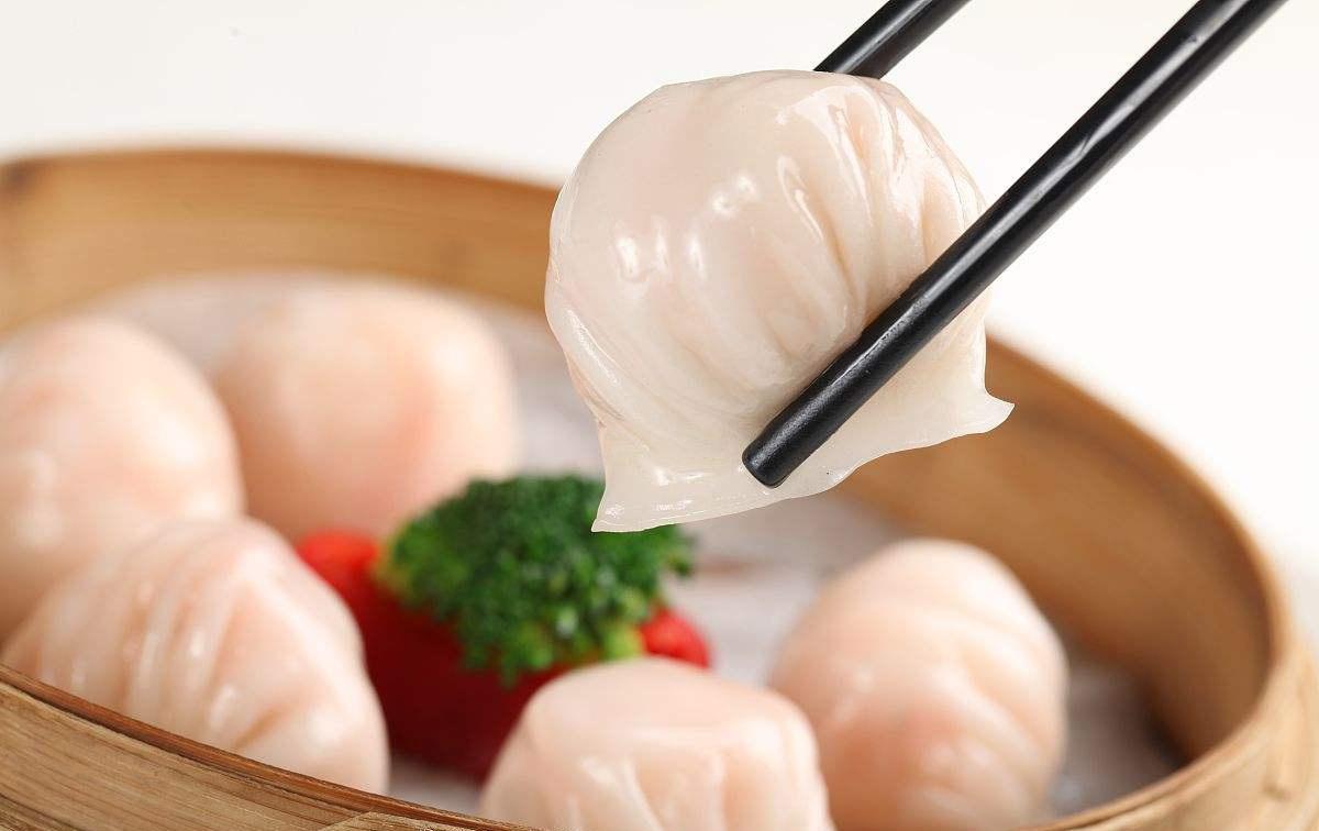 A translucent har gow dumpling lifted by chopsticks