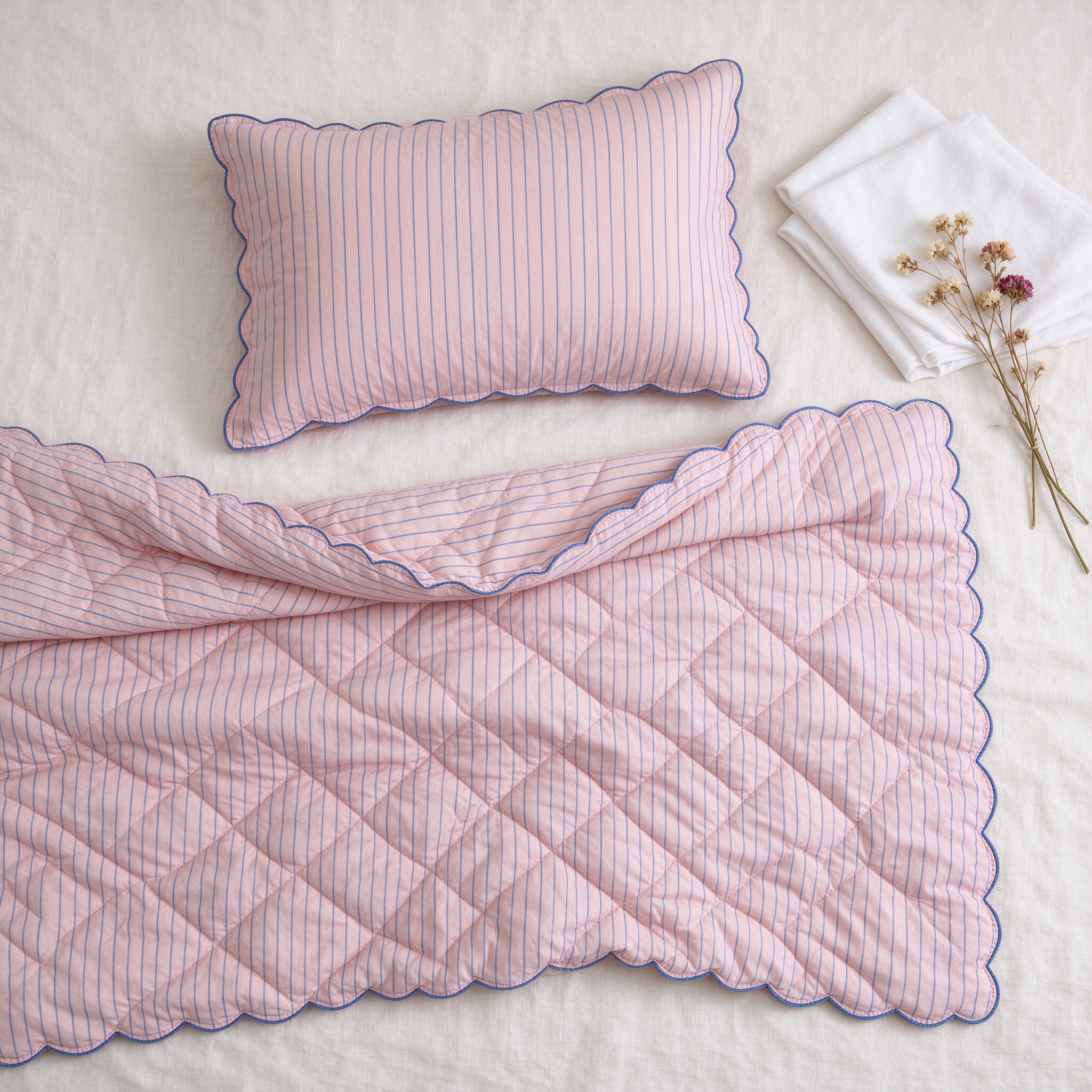 Quilted blush bedding with fine blue pinstripe, flat lay